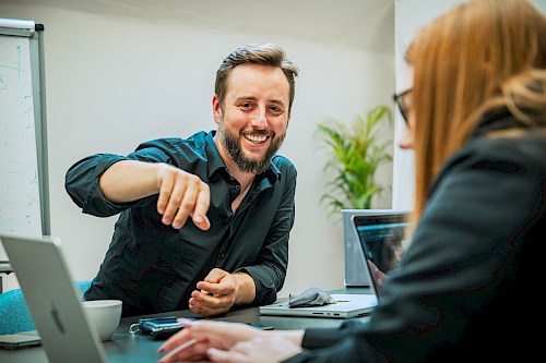 Man and woman with computers in meeting room, man smiling and pointing at screen